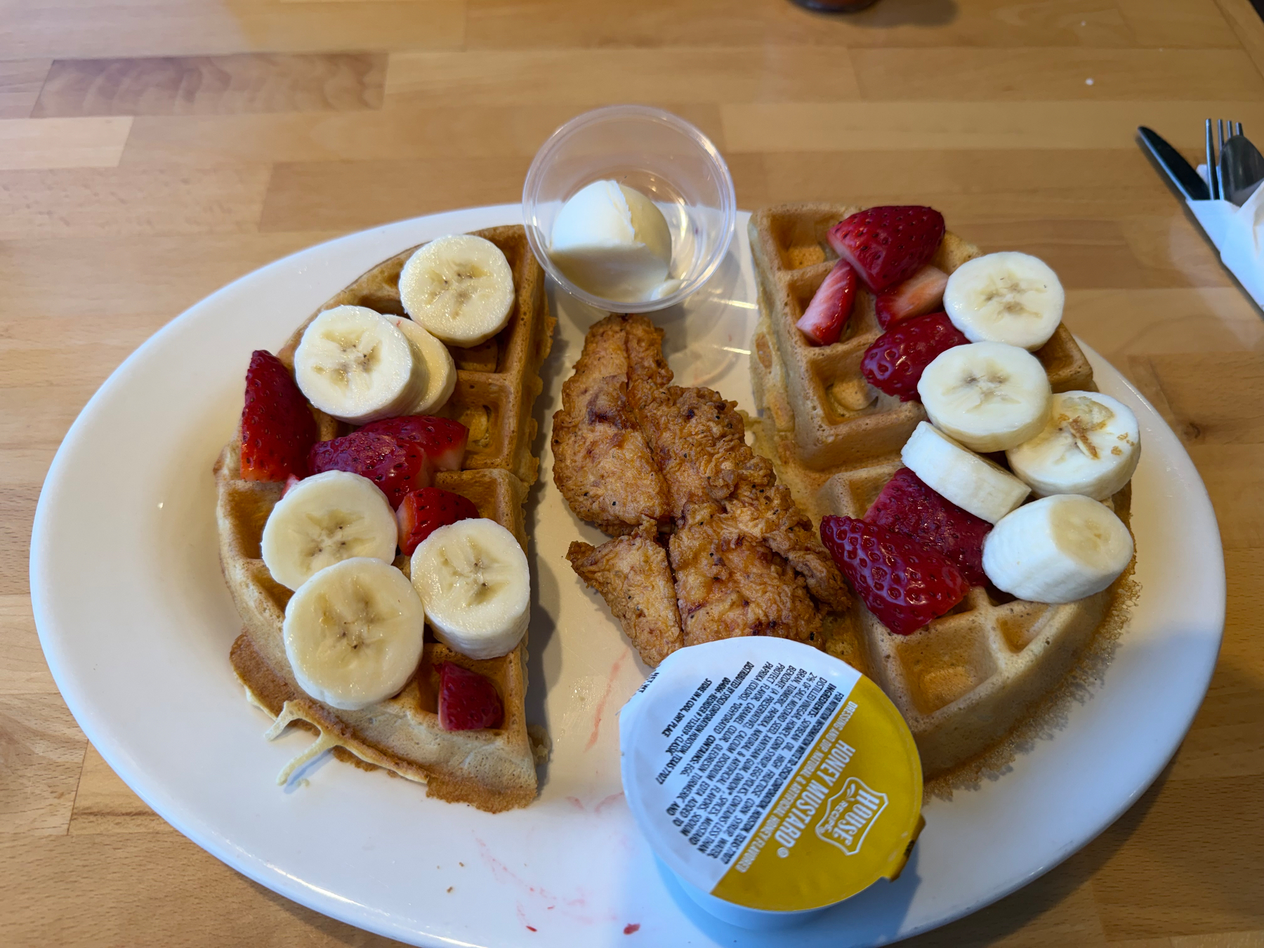A Belgian waffle (with sliced strawberries and bananas on top) that has been split in half with a piece of fried chicken in the middle.