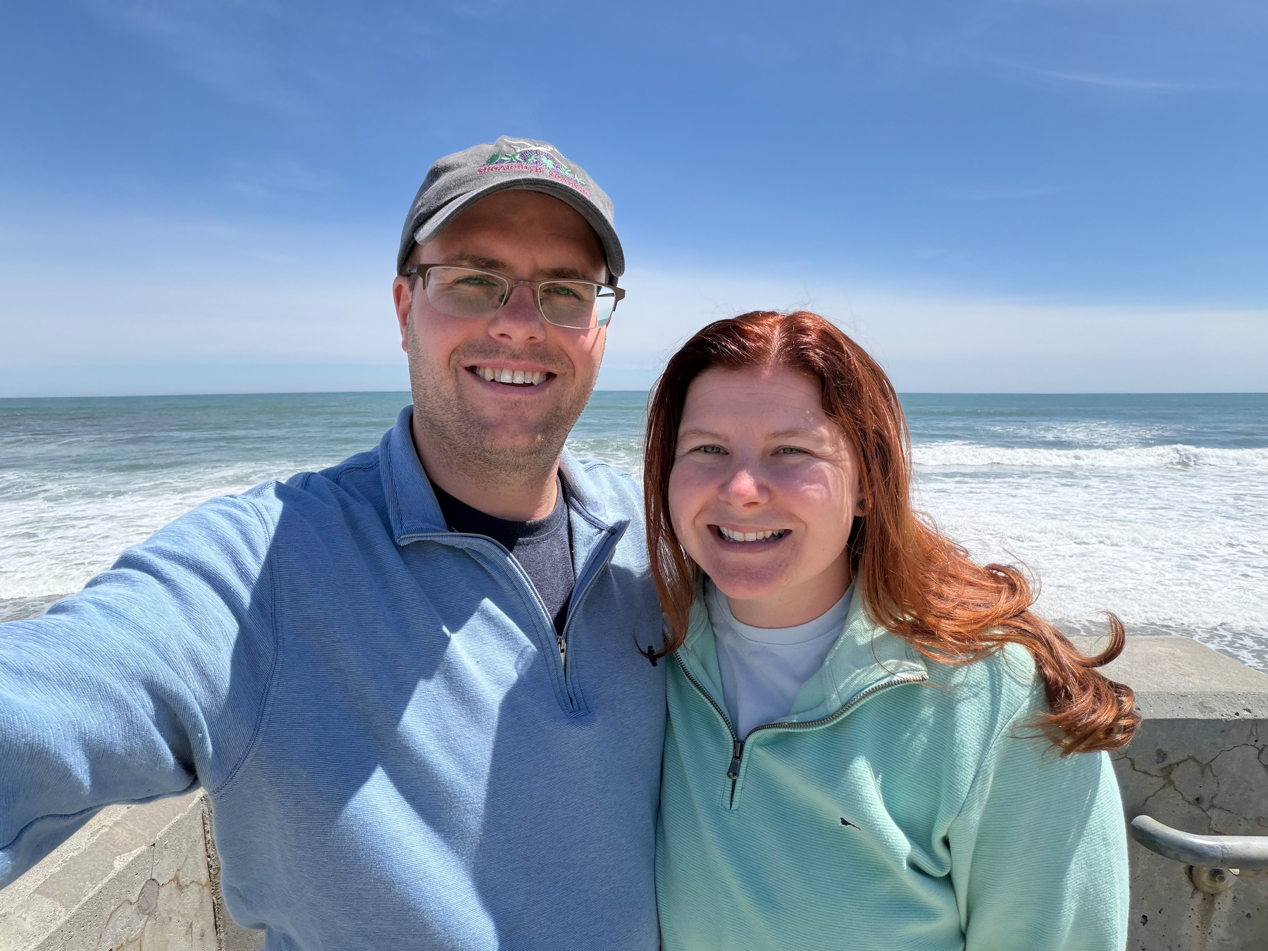 Zeba and I standing in front of the ocean at the beach, with blue sky and the ocean with some waves in the background.